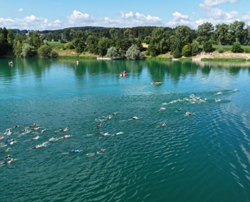 Blick auf See mit Schwimmern. Ufer und Landschaft im Hintergrund