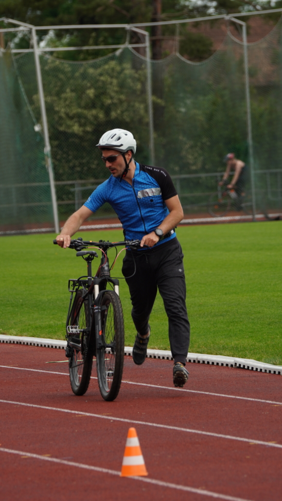 Sportler schiebt Rad auf Sportanlage