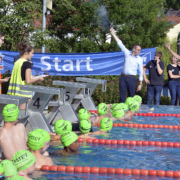 Kinder mit grünen Bademützen in Schwimmbad; Mann gibt Startschuss