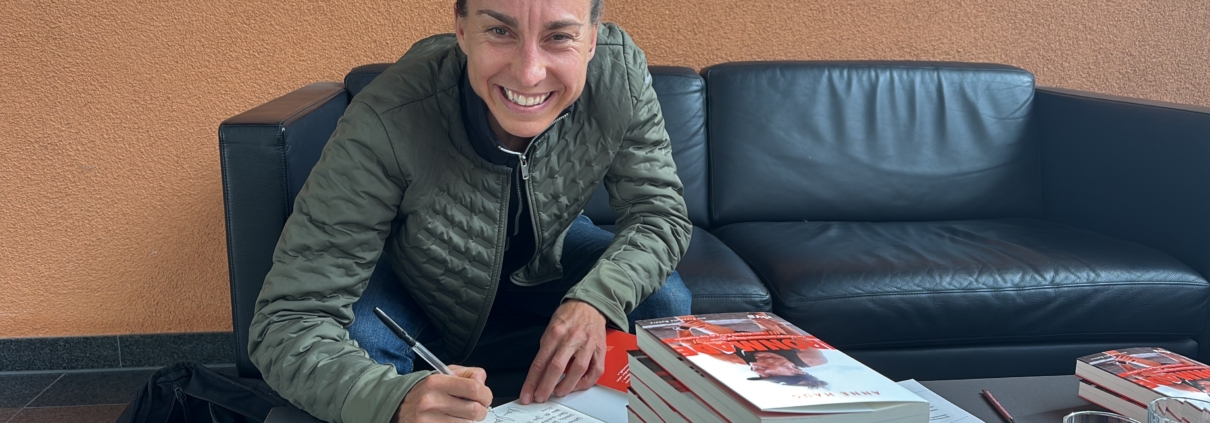 Portrait einer lachenden Frau mit Stapel Bücher