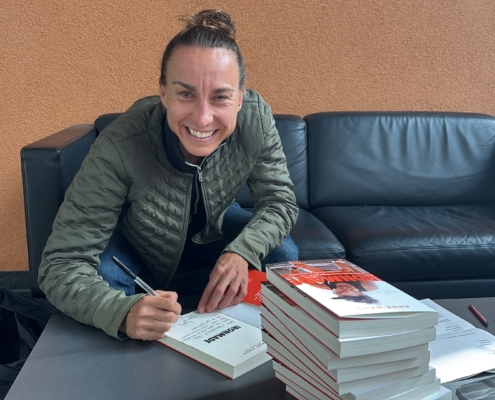Portrait einer lachenden Frau mit Stapel Bücher