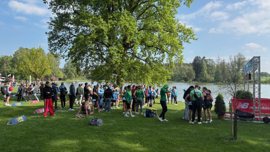 Eventgelände mit grüner Wiese, Menschen und See im Hintergrund