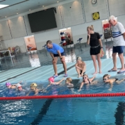 Kinder im Schwimmbecken und drei Trainer an Land