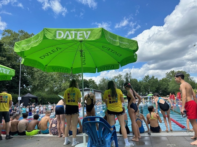 Freibad mit vielen Menschen und grünem Schirm